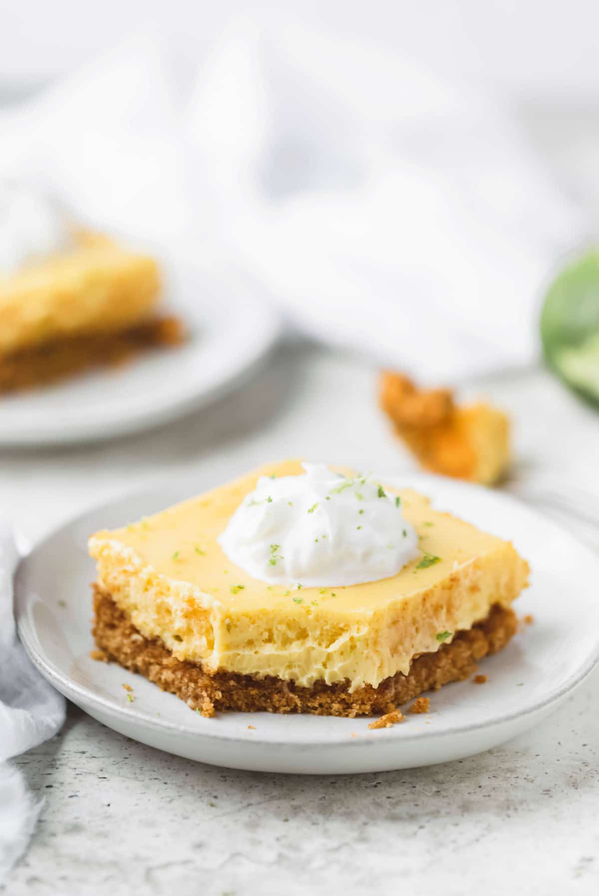 Piece of key lime pie bars topped with whipped cream and lime zest