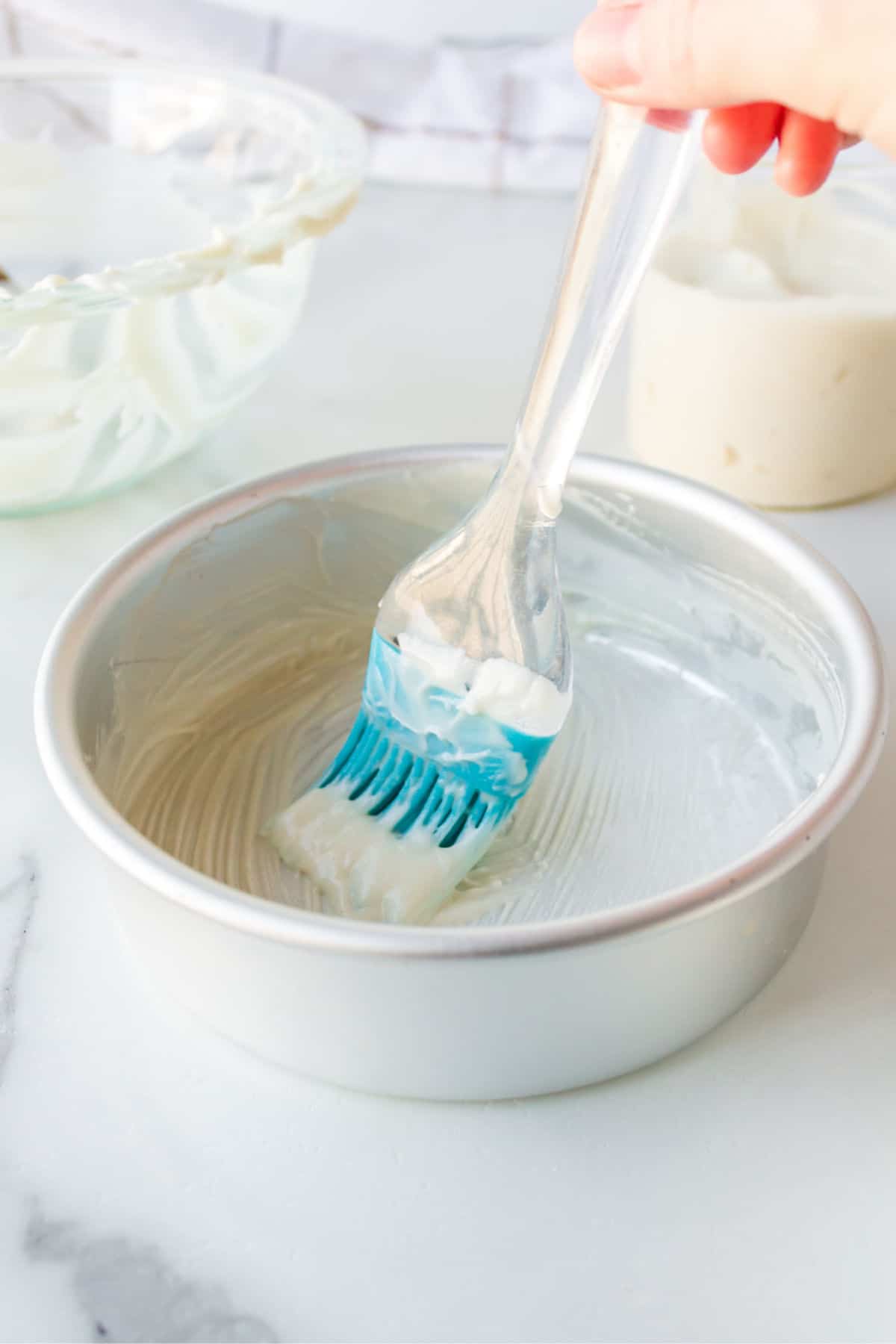 Silicone pastry brush brushing pan release onto a round cake pan. 