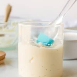 A half filled glass jar of pan release with a silicone baking brush in it.