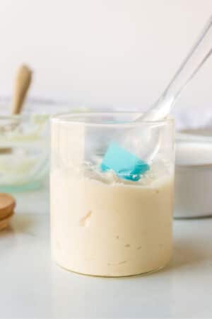 A half filled glass jar of pan release with a silicone baking brush in it.