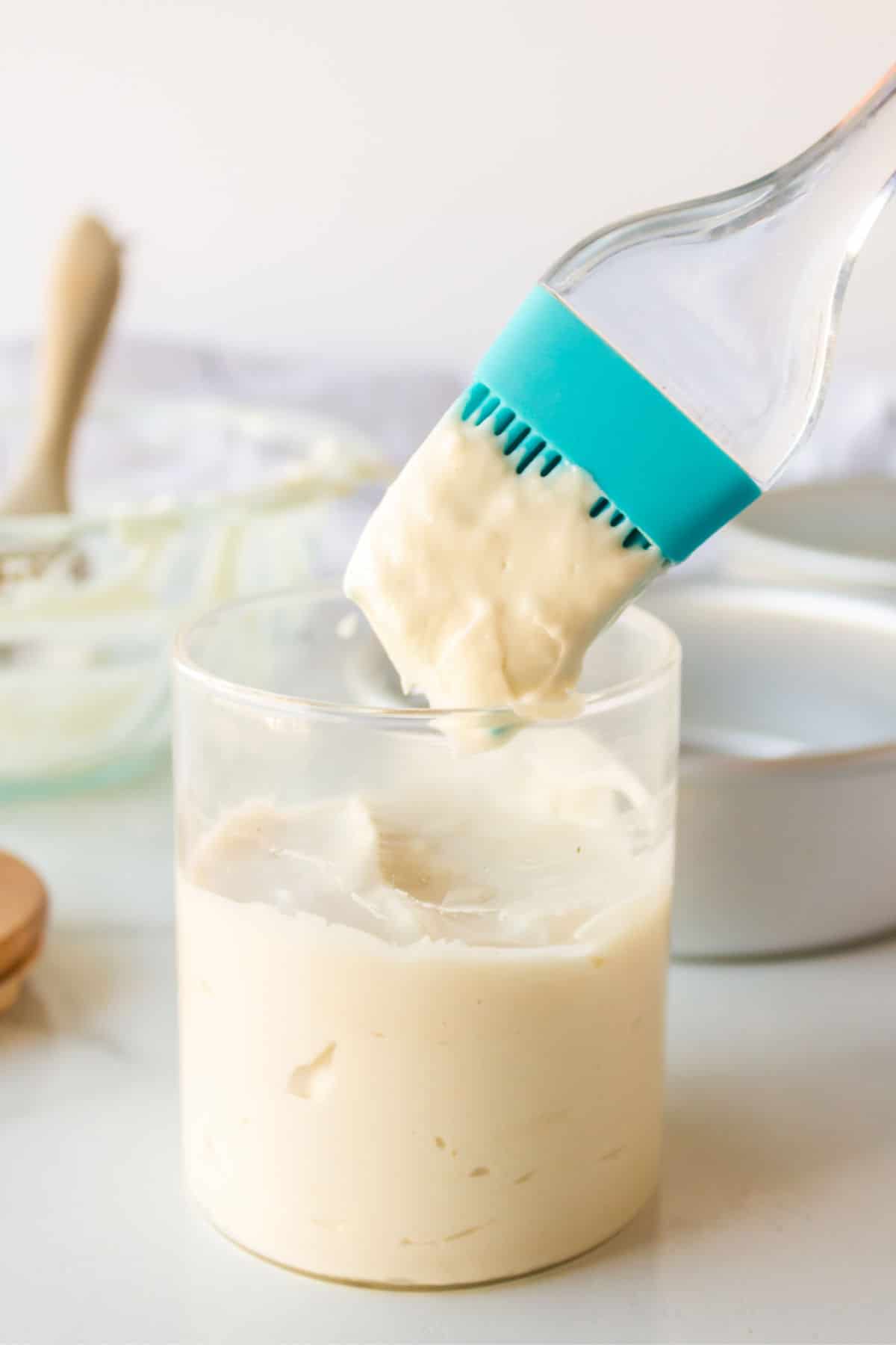 A silicone pastry brush dipping into a jar of pan release. 