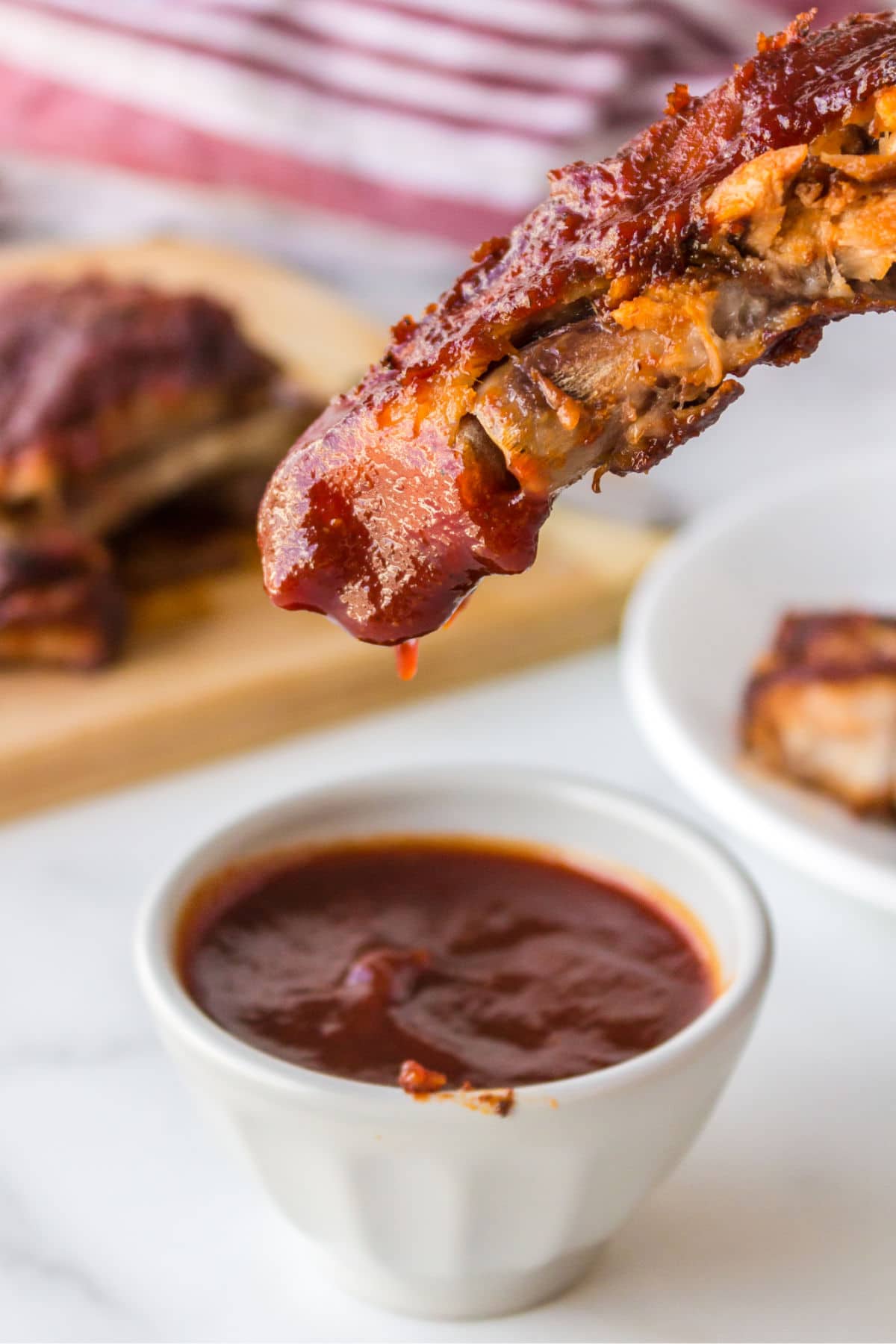 Rib dipping into a white cup full of bbq sauce. 