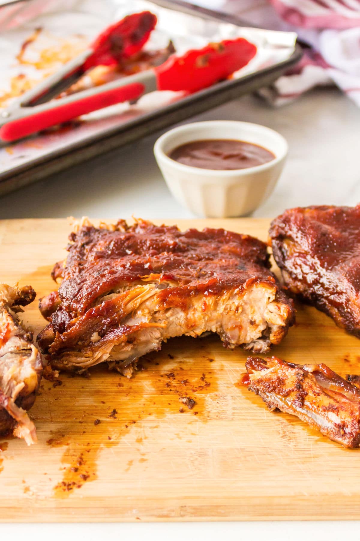 Ribs on a wooden cutting board next to a white dish with bbq sauce. 