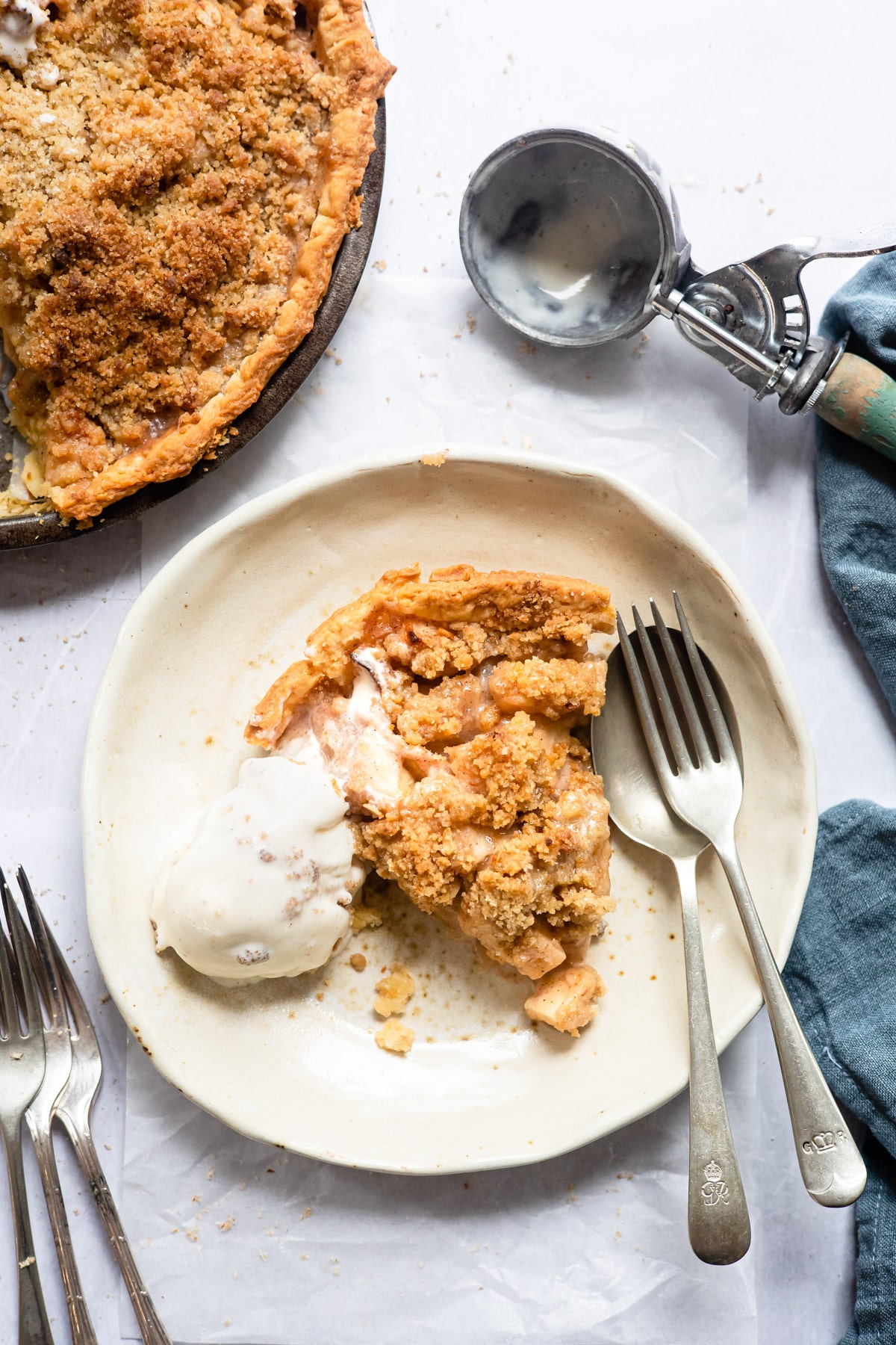 Slice of apple crumb pie next to a scoop of vanilla ice cream on a plate. 