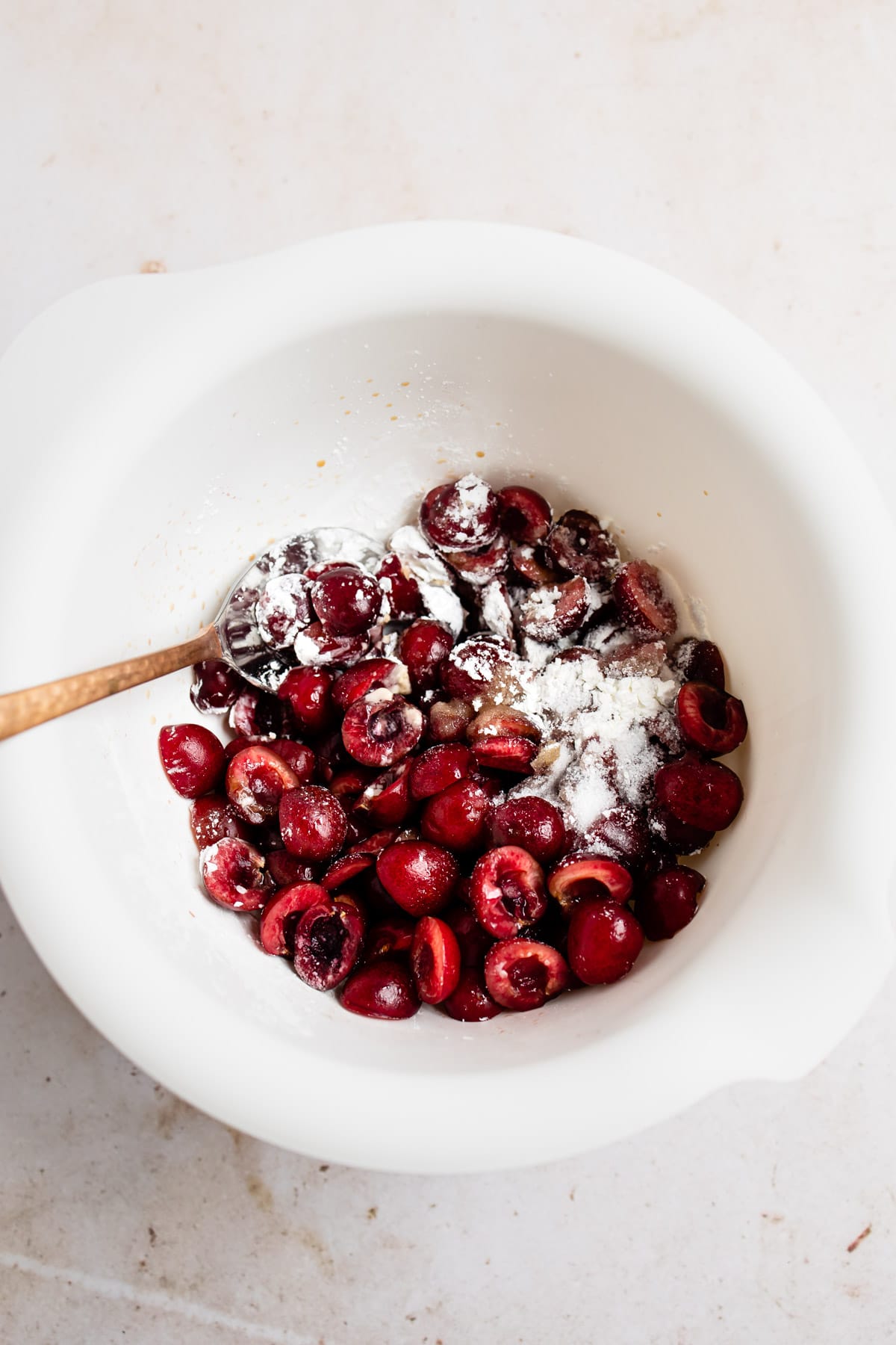 Cherries and sugar and cornstarch in a white mixing bowl. 