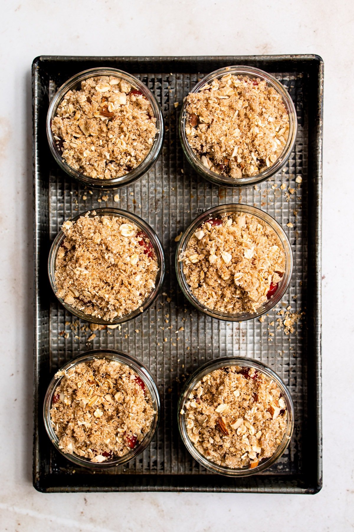 6 unbaked cherry crisps in ramekins on a baking sheet.