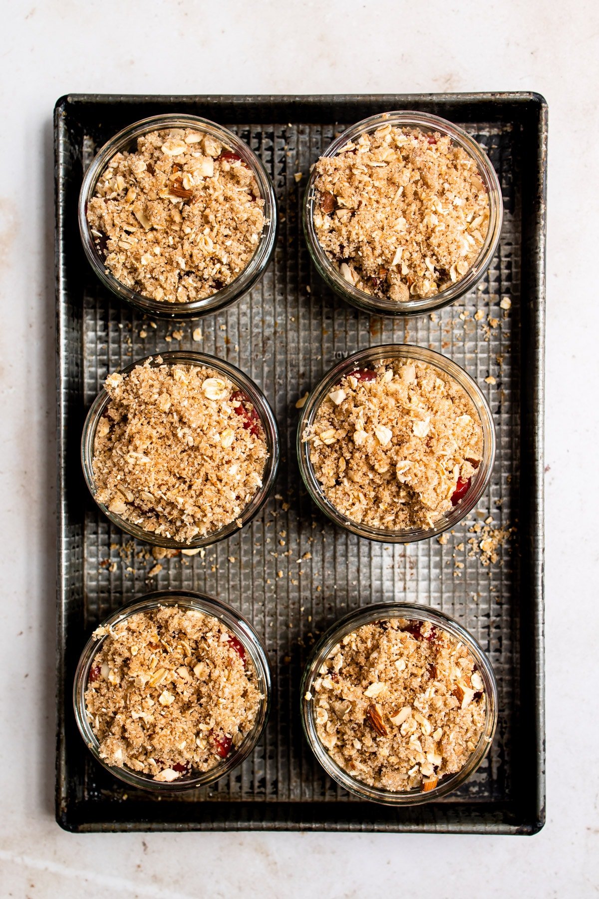 6 unbaked cherry crisps in ramekins on a baking sheet. 