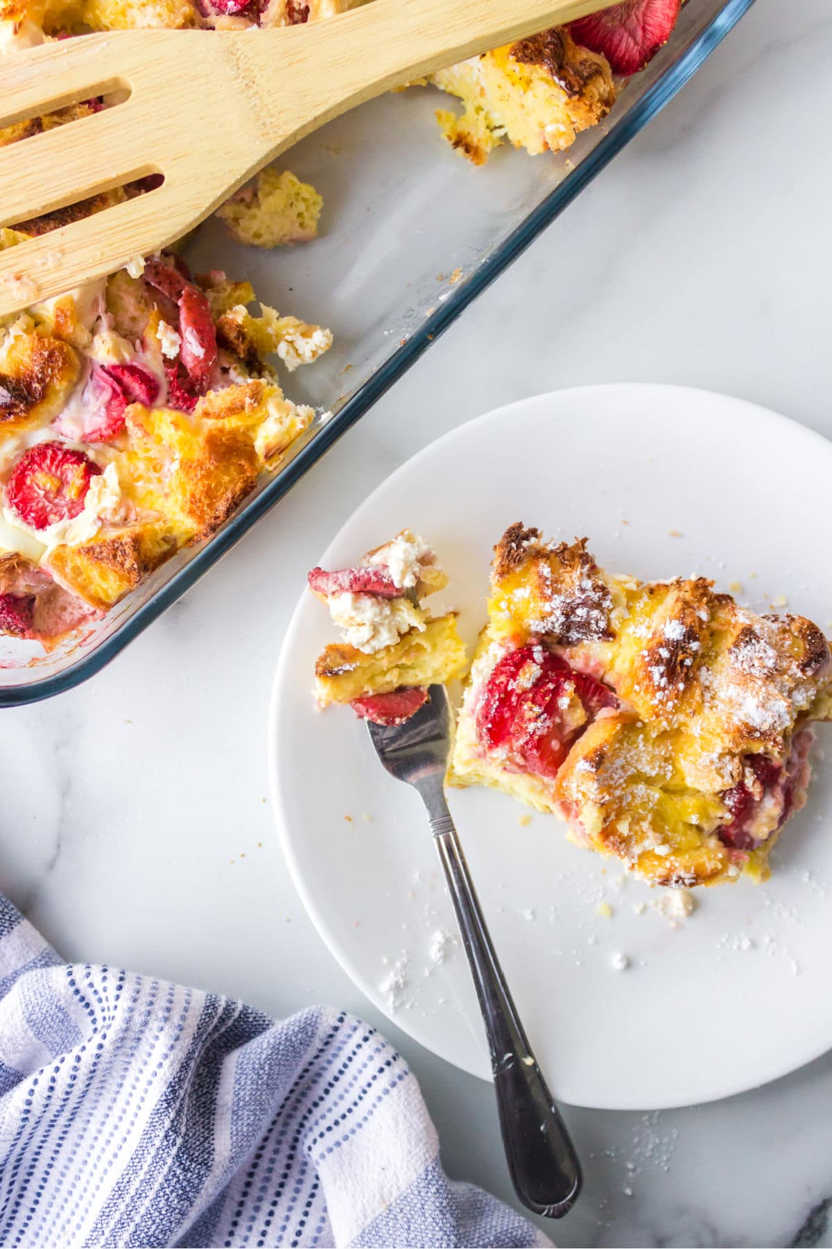 Slice of strawberry cream cheese French toast on a white plate with a bite on a fork.