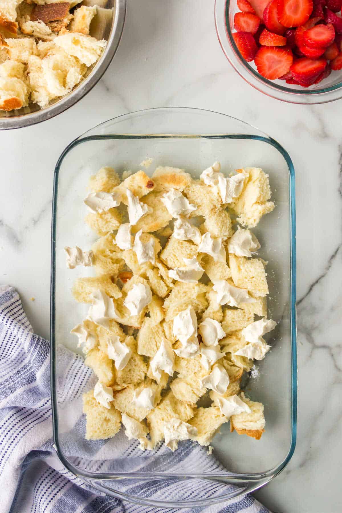 Cream cheese cubes over bread cubes in a glass baking dish. 