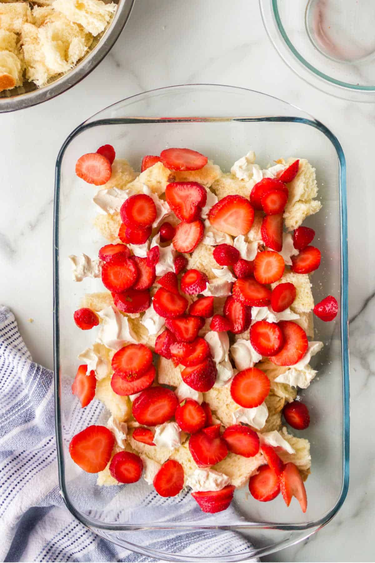 Sliced strawberries over bread cubes in a glass baking dish. 