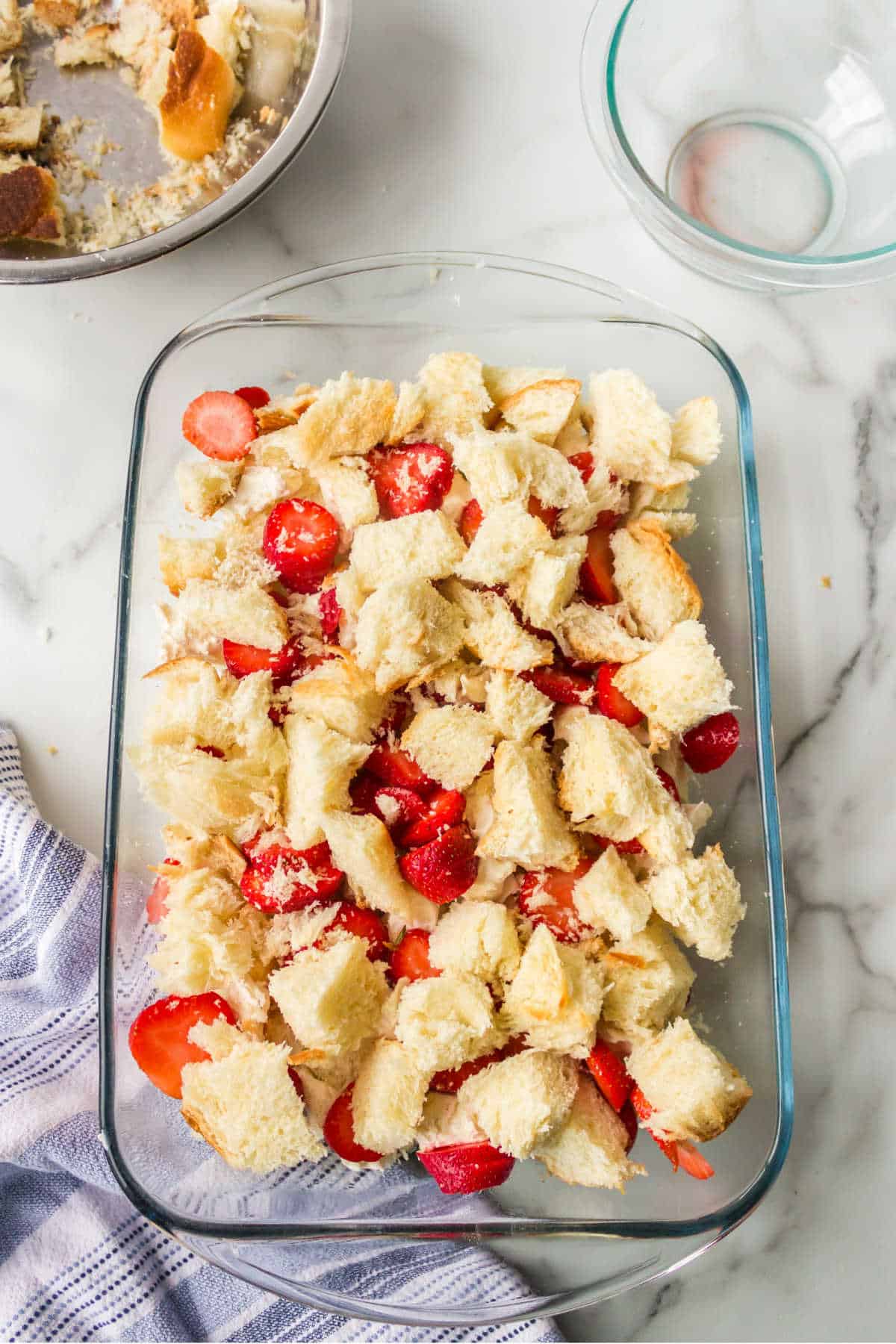 Bread cubes covering sliced strawberries in a glass baking dish. 