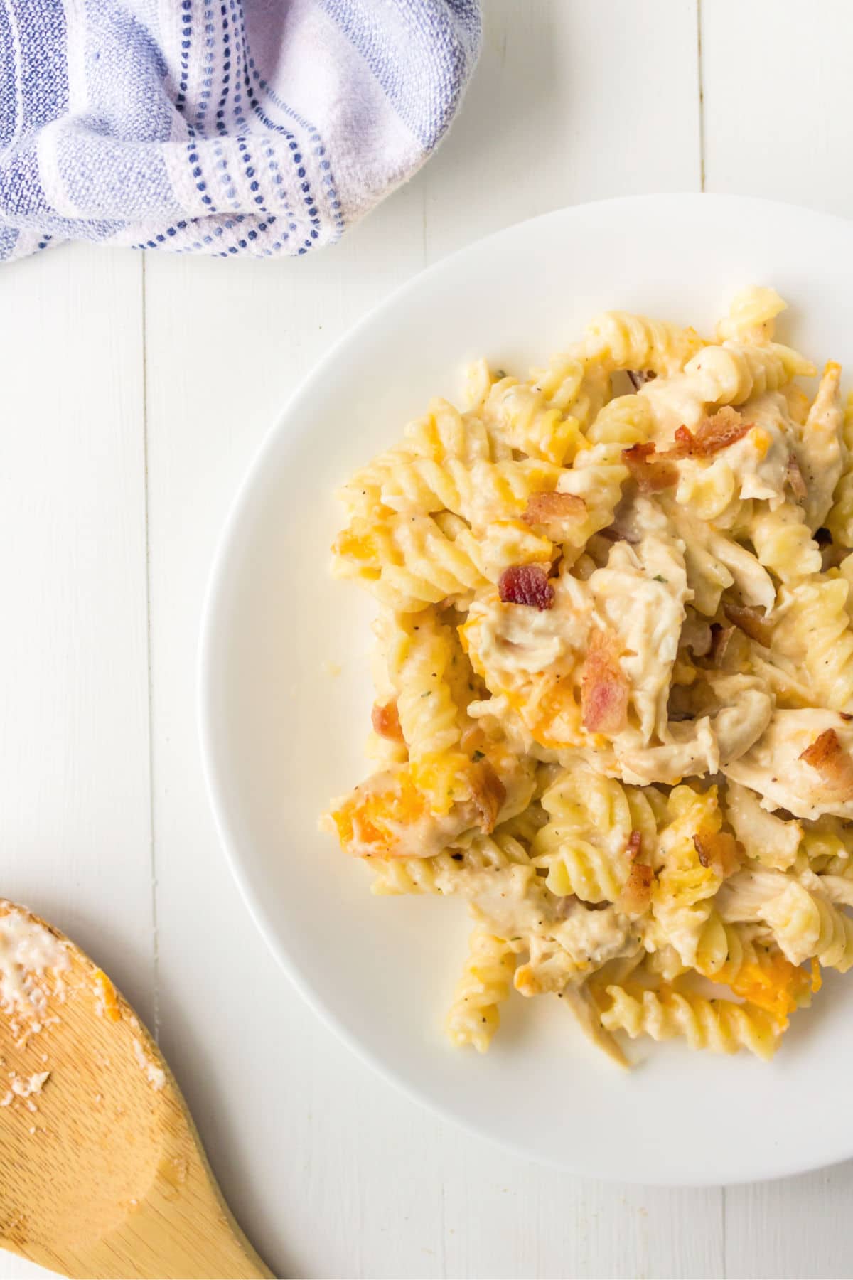 White plate of chicken bacon ranch pasta next to a blue napkin and wooden spoon.