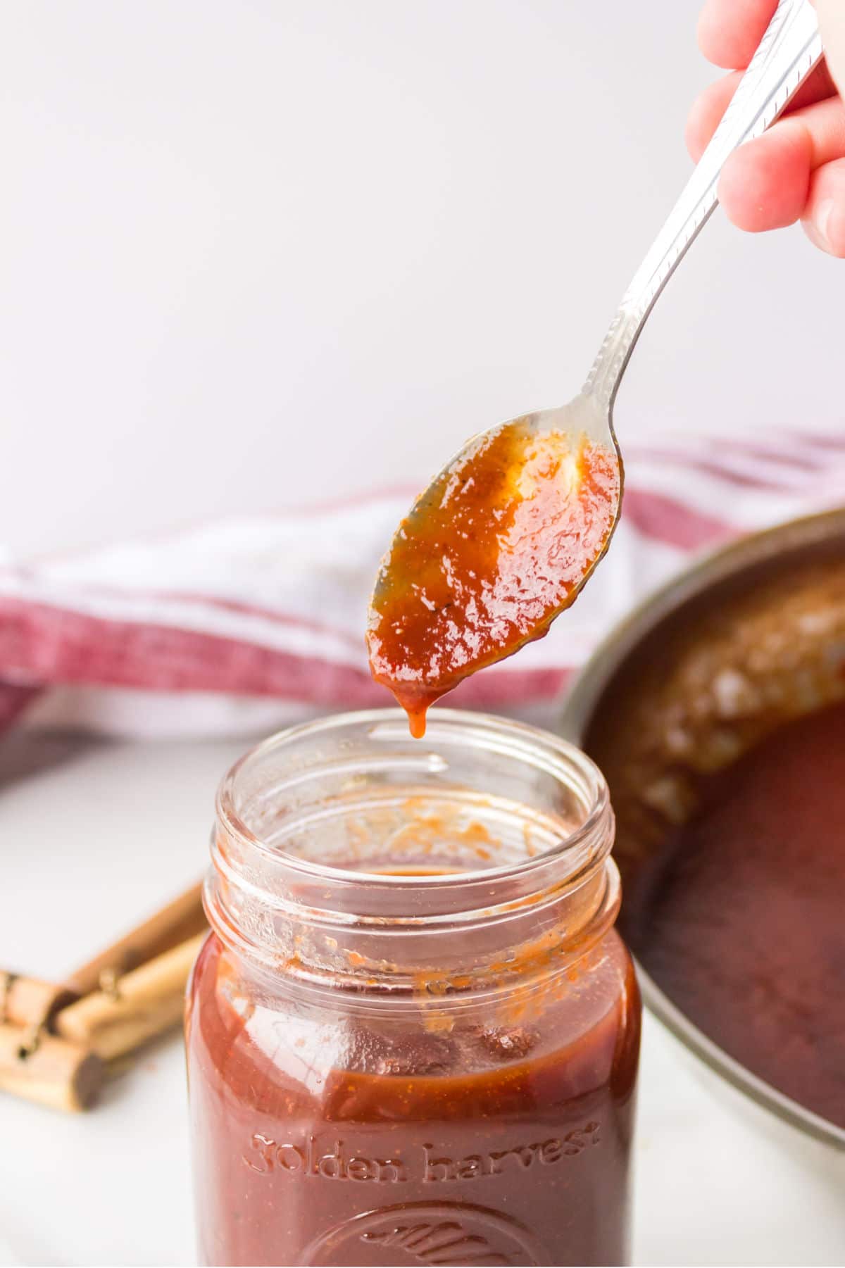 Dr Pepper barbecue sauce pouring off a spoon into a jar.