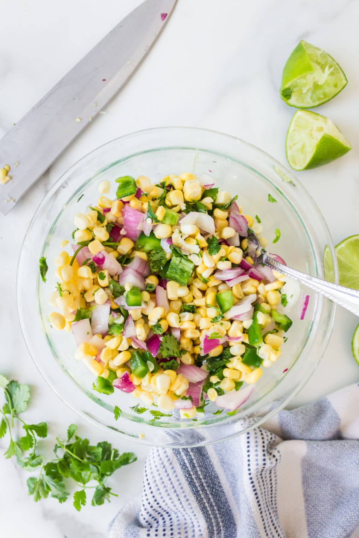 Corn salsa in a glass dish with fresh limes and fresh cilantro around it. 