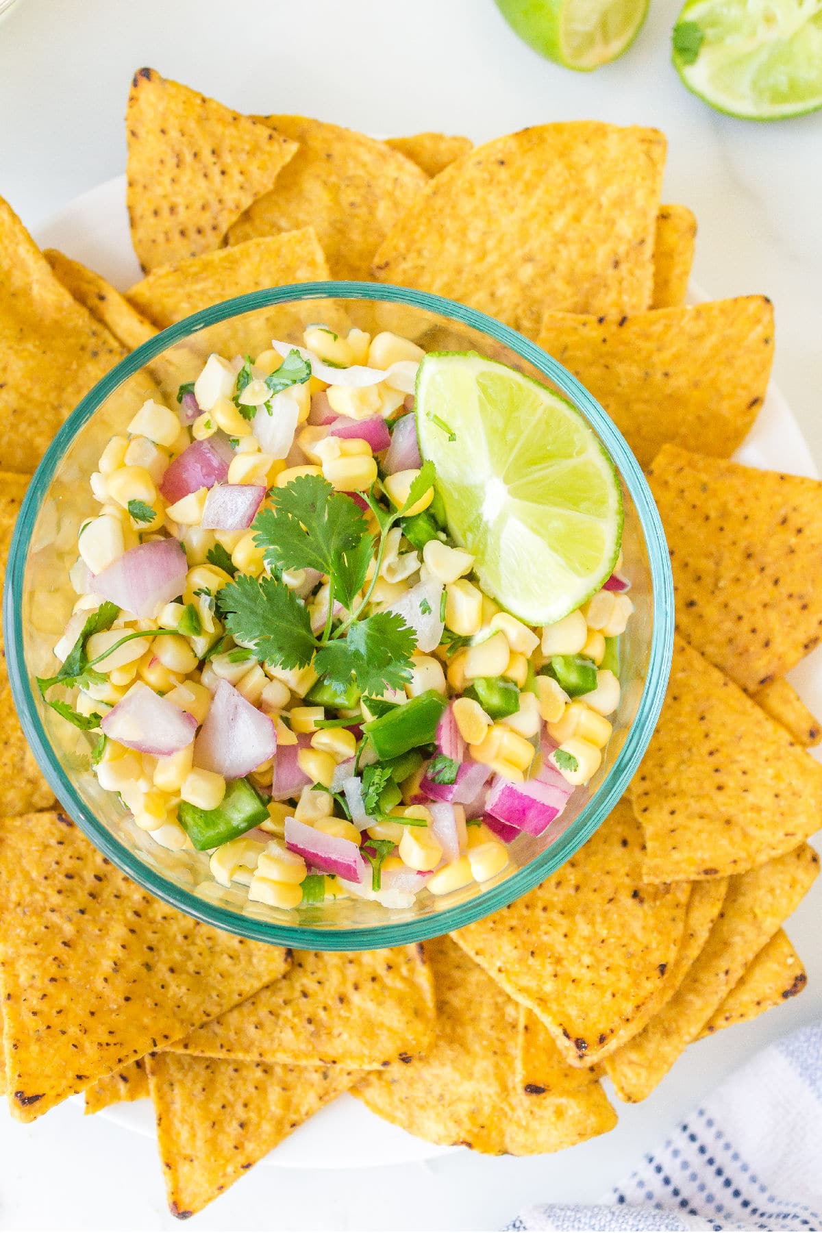 Glass bowl full of corn salsa topped with a lime wedge and fresh cilantro.