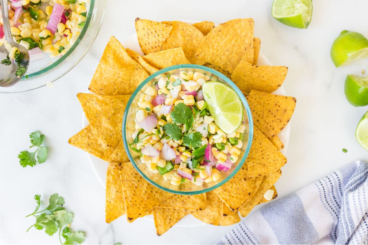 Dish of corn salsa next to sliced limes and cilantro.