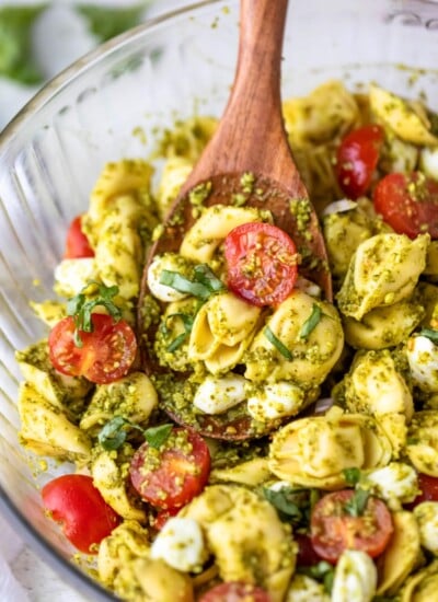 wooden spoon scooping pesto tortellini pasta salad.