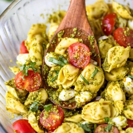 wooden spoon scooping pesto tortellini pasta salad.