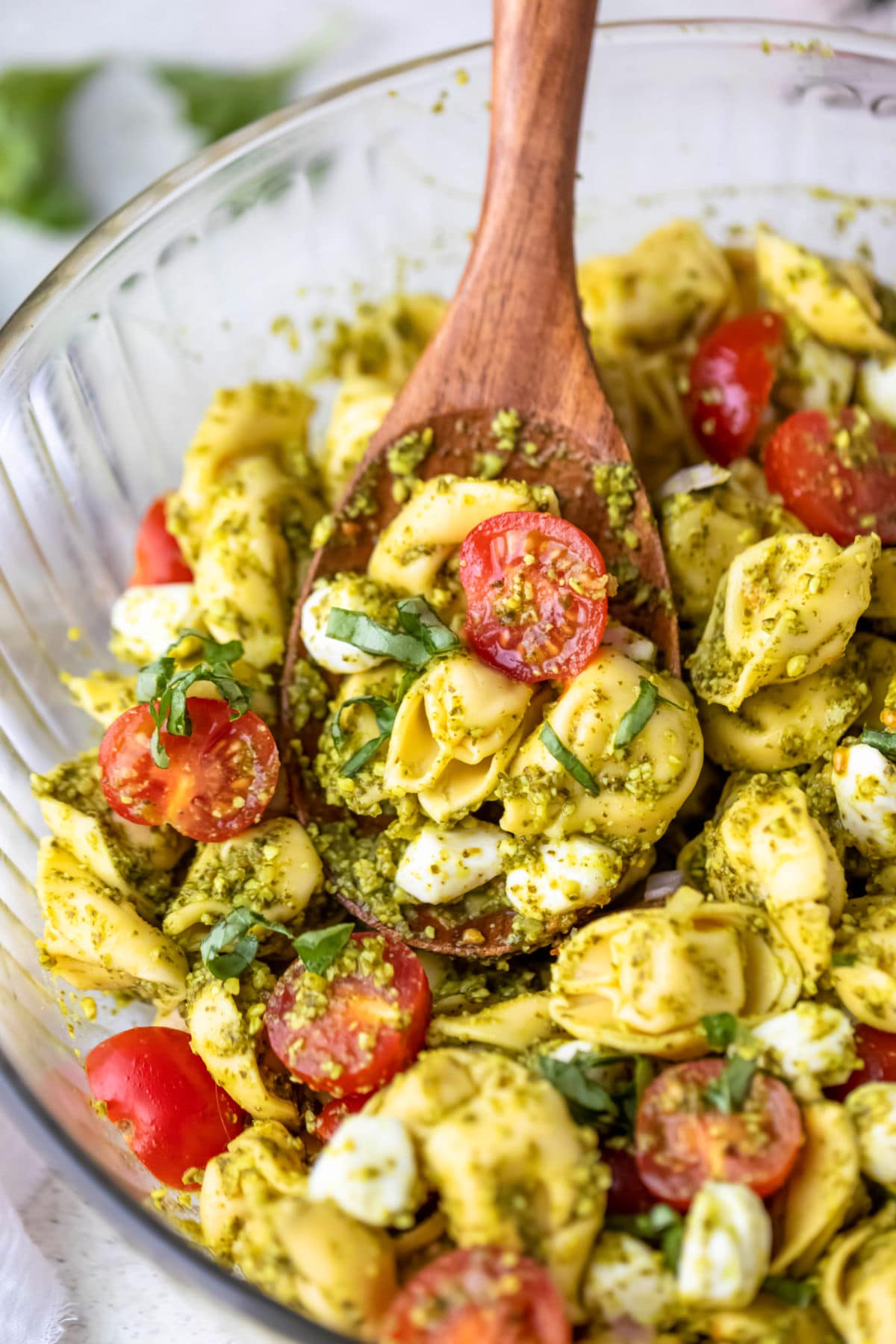 wooden spoon scooping pesto tortellini pasta salad. 