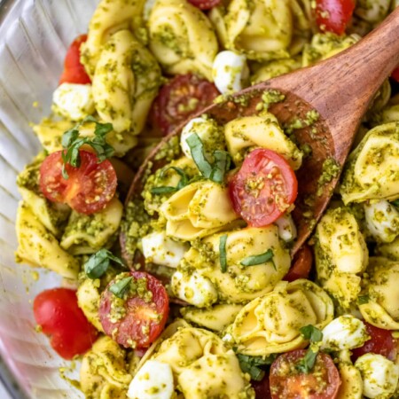 Close up photo of pesto tortellini pasta salad on a wooden spoon.