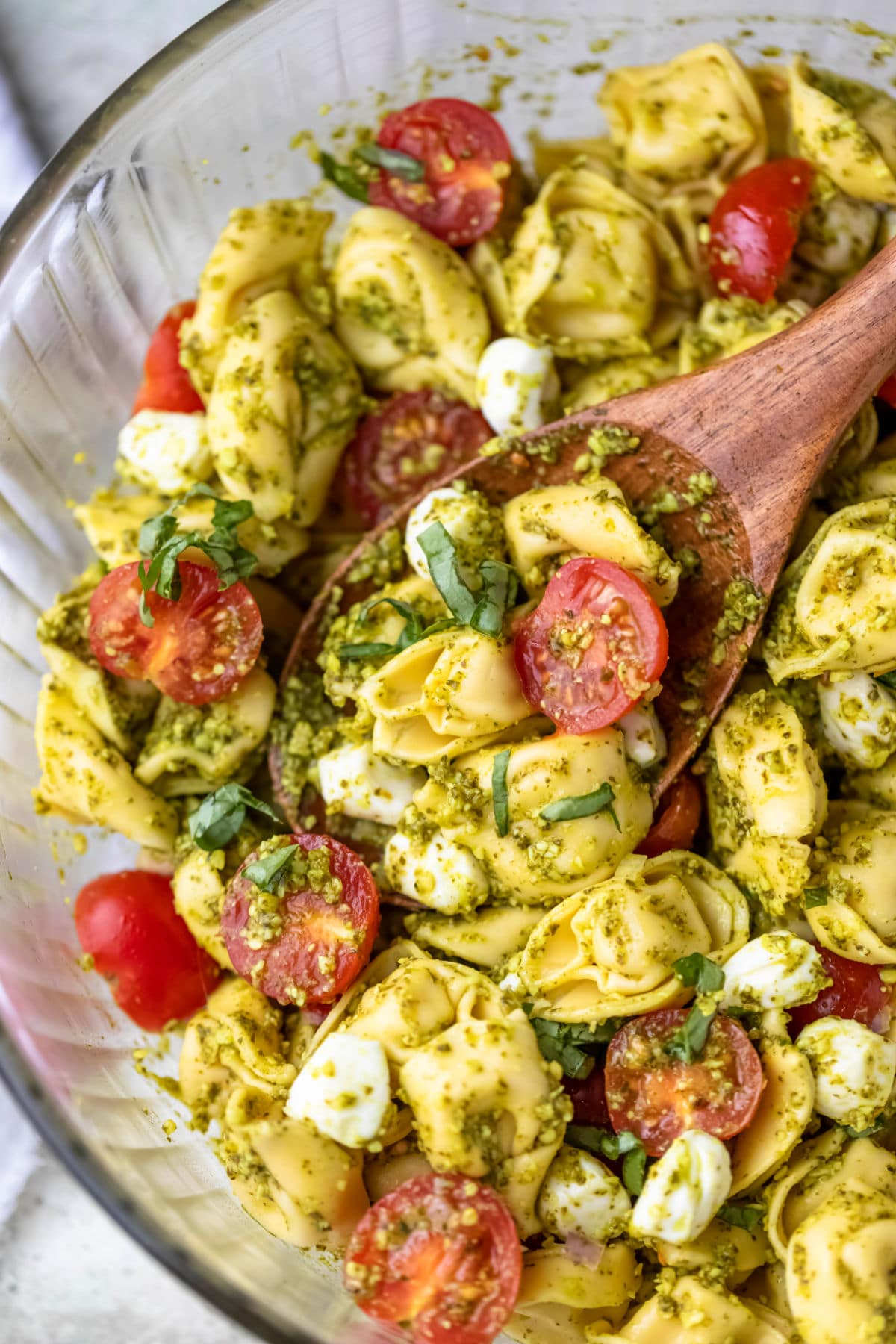 Close up photo of pesto tortellini pasta salad on a wooden spoon.