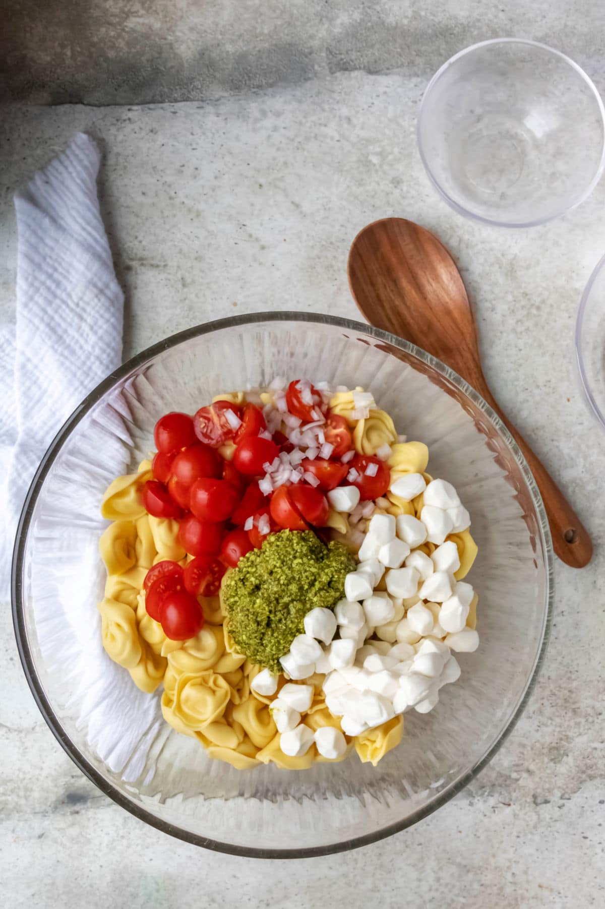 Pesto tortellini pasta salad ingredients in a glass mixing bowl. 