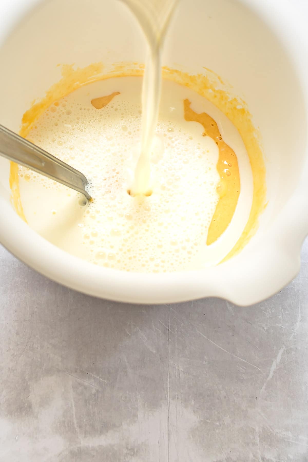 Milk streaming into egg yolk mixture.