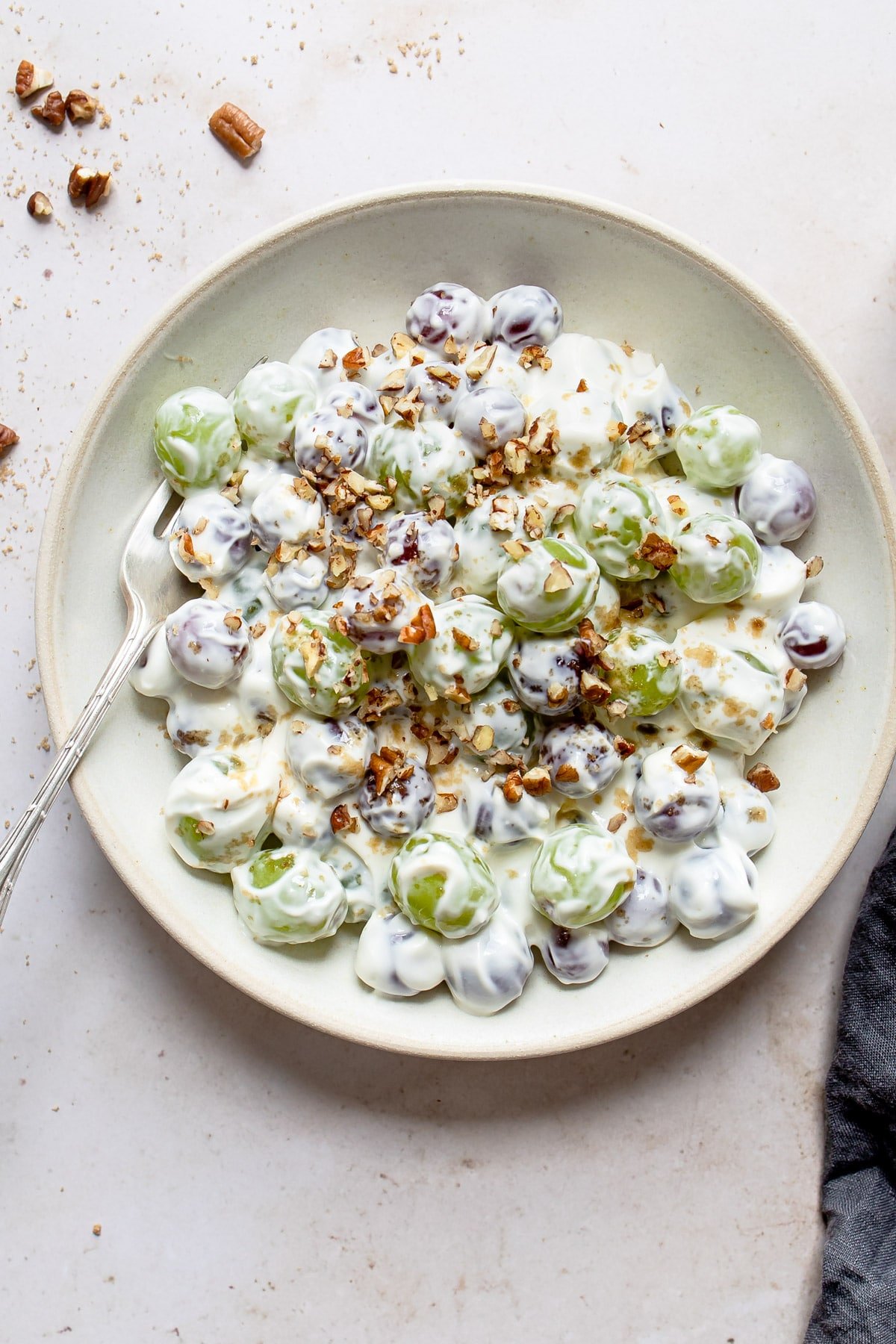 A plate of grape salad next to a few chopped pecans. 