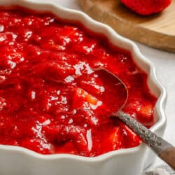 A dish of homemade strawberry sauce next to fresh strawberries.
