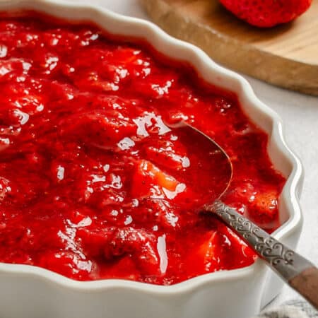 A dish of homemade strawberry sauce next to fresh strawberries.