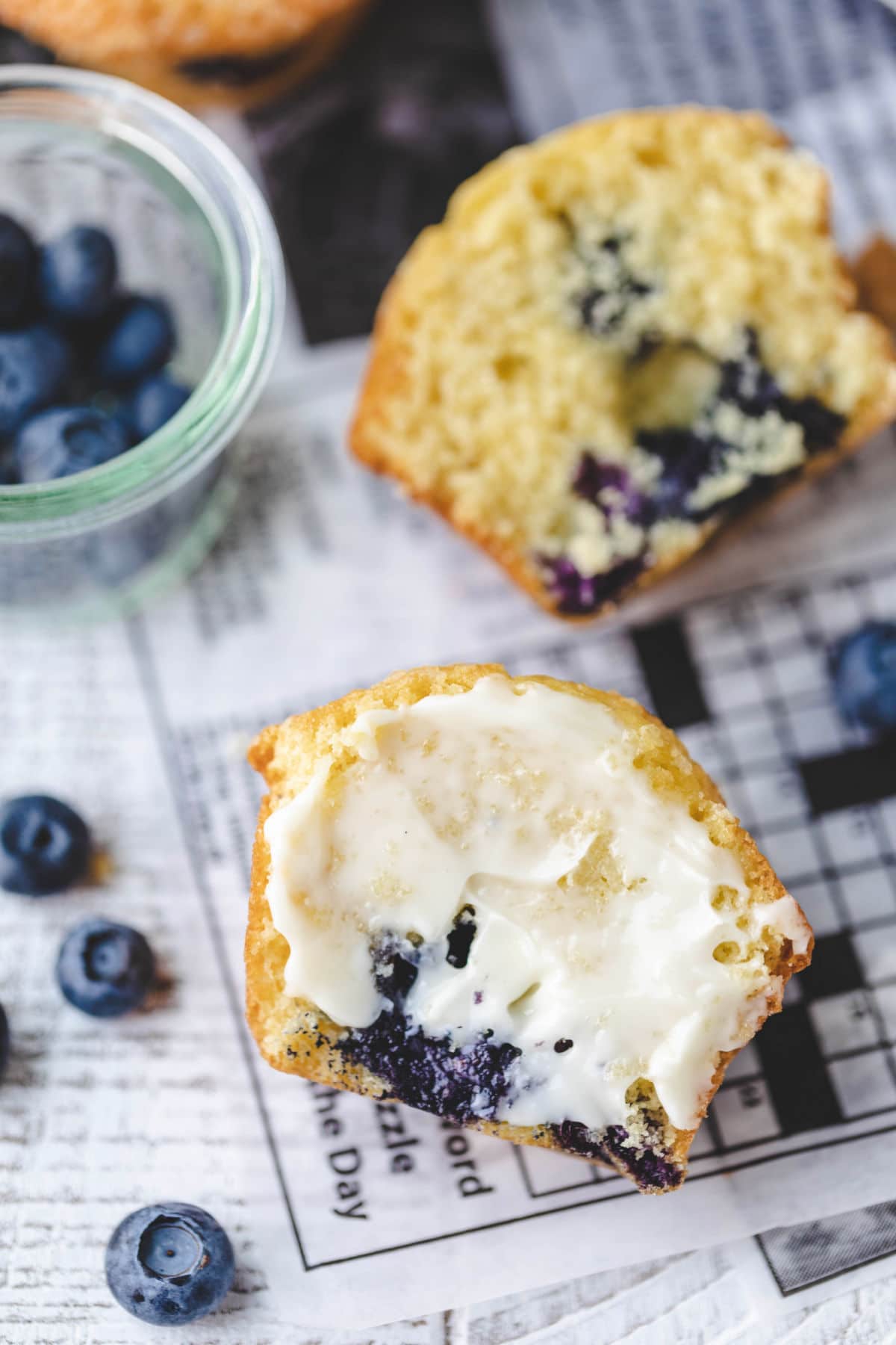Bakery Style Blueberry Muffins Buttered half of a blueberry muffin on a piece of deli paper.