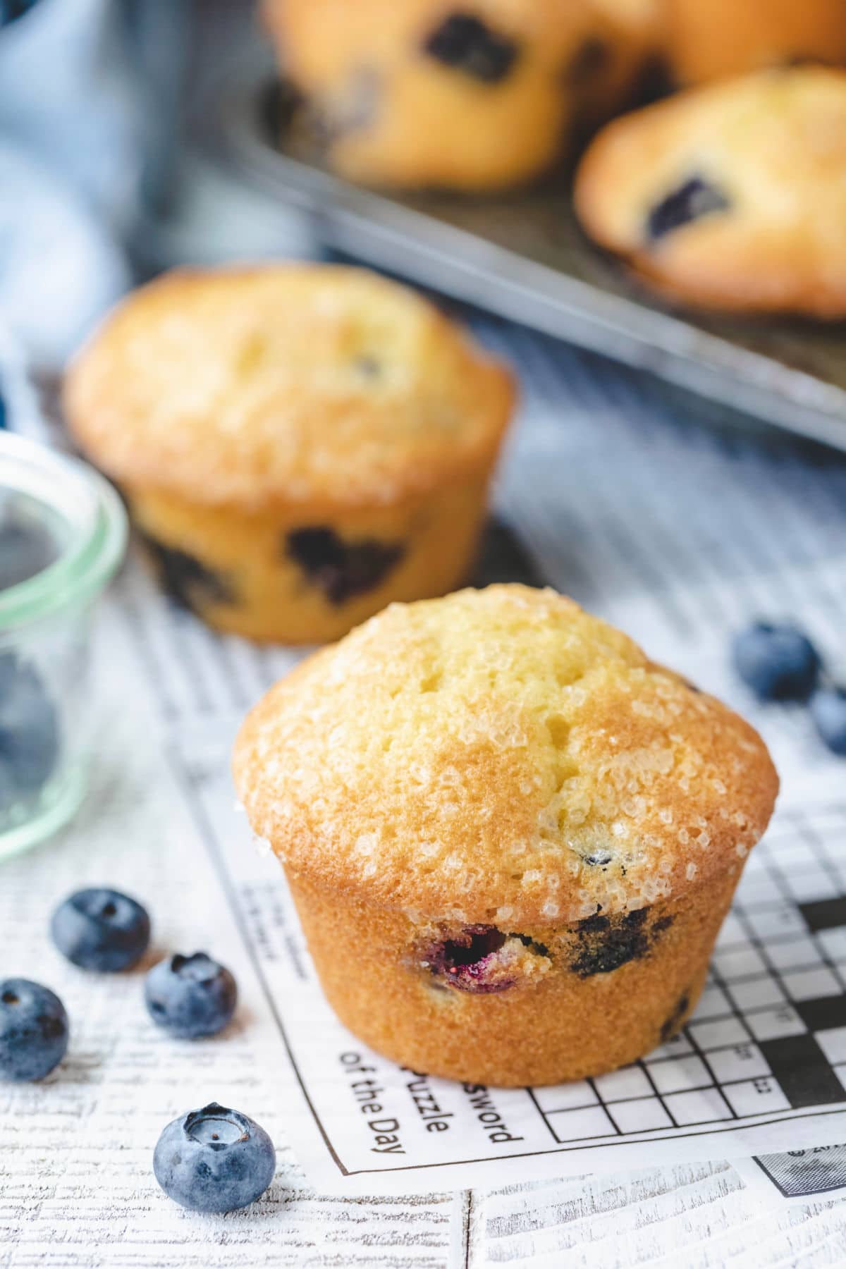 Bakery Style Blueberry Muffins Blueberry muffins on a piece of deli paper with blueberries scattered around them.
