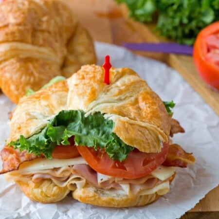 California club croissant sandwich next to a sliced tomato.