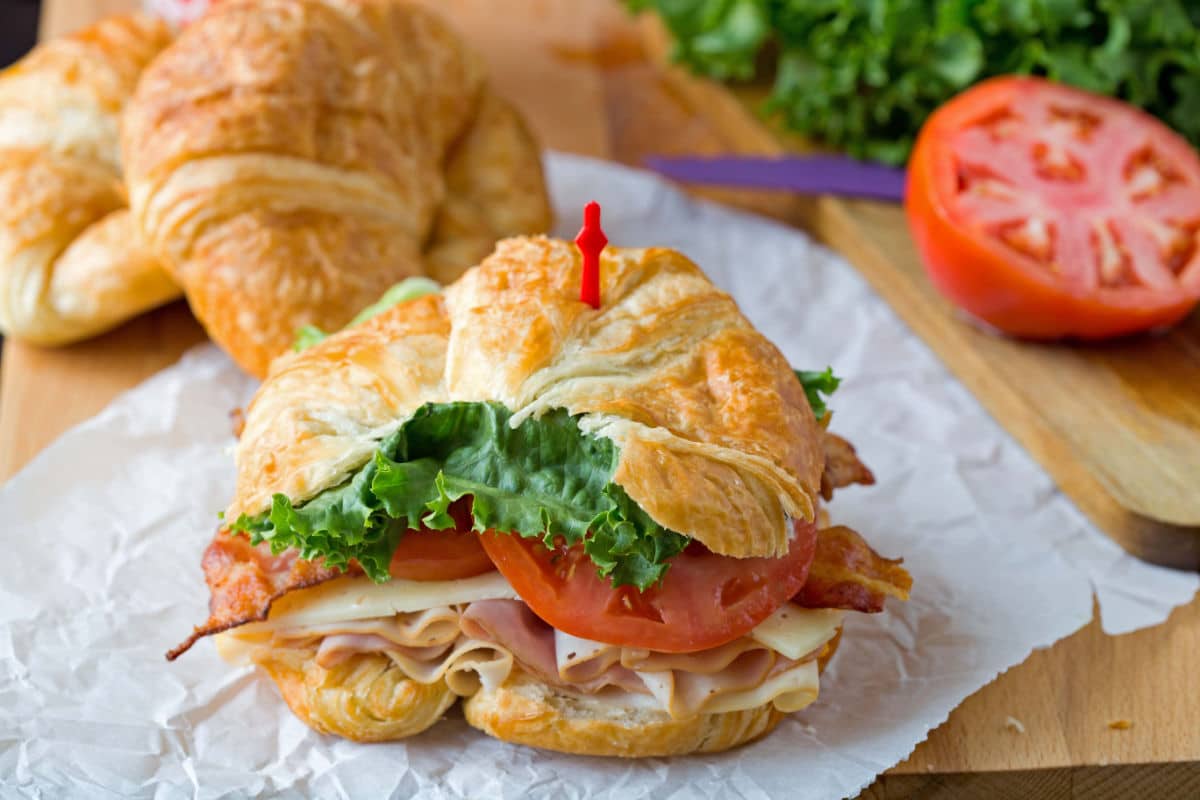 California club croissant sandwich next to a sliced tomato. 