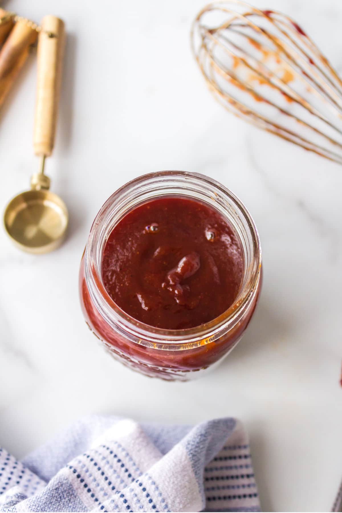 Kansas city bbq sauce in a jar next to a whisk. 