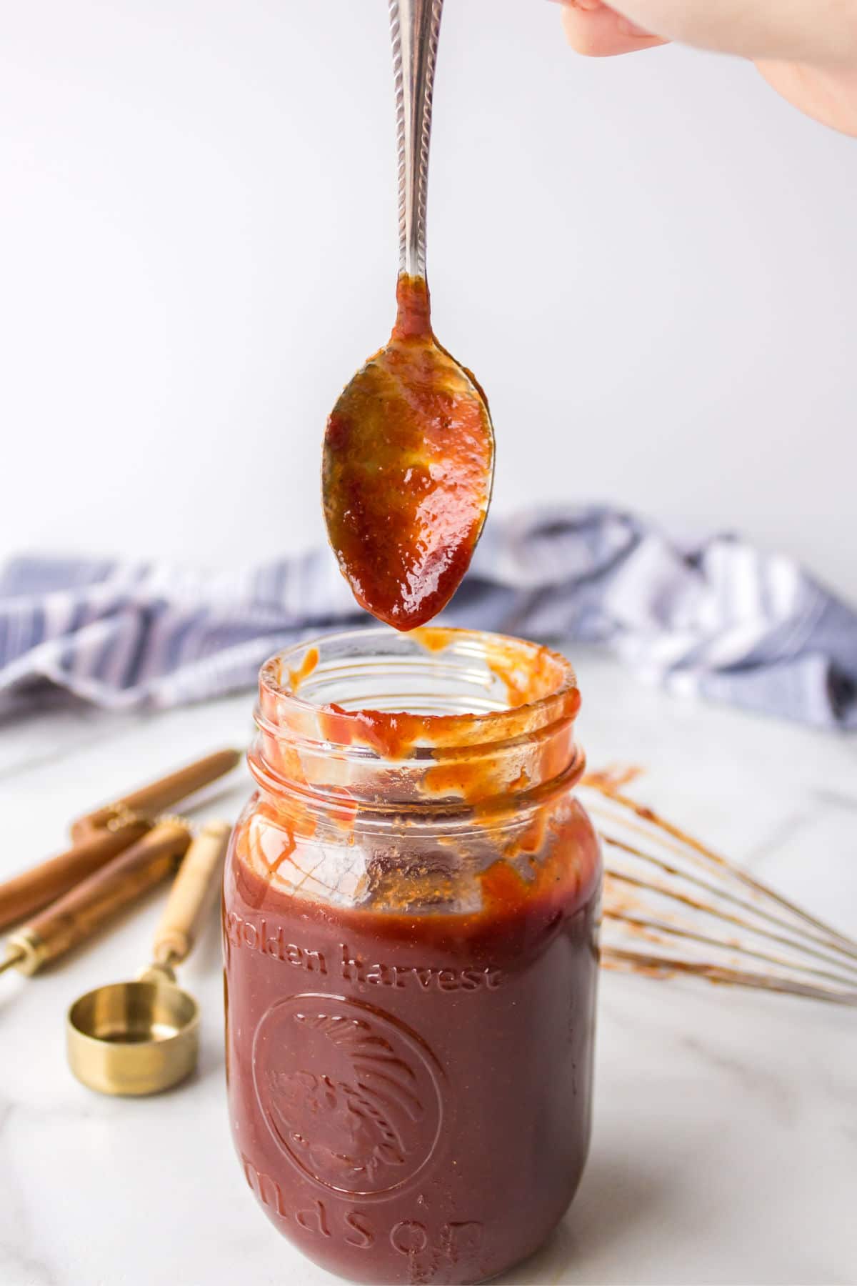 A spoon coming out of a jar of barbecue sauce. 