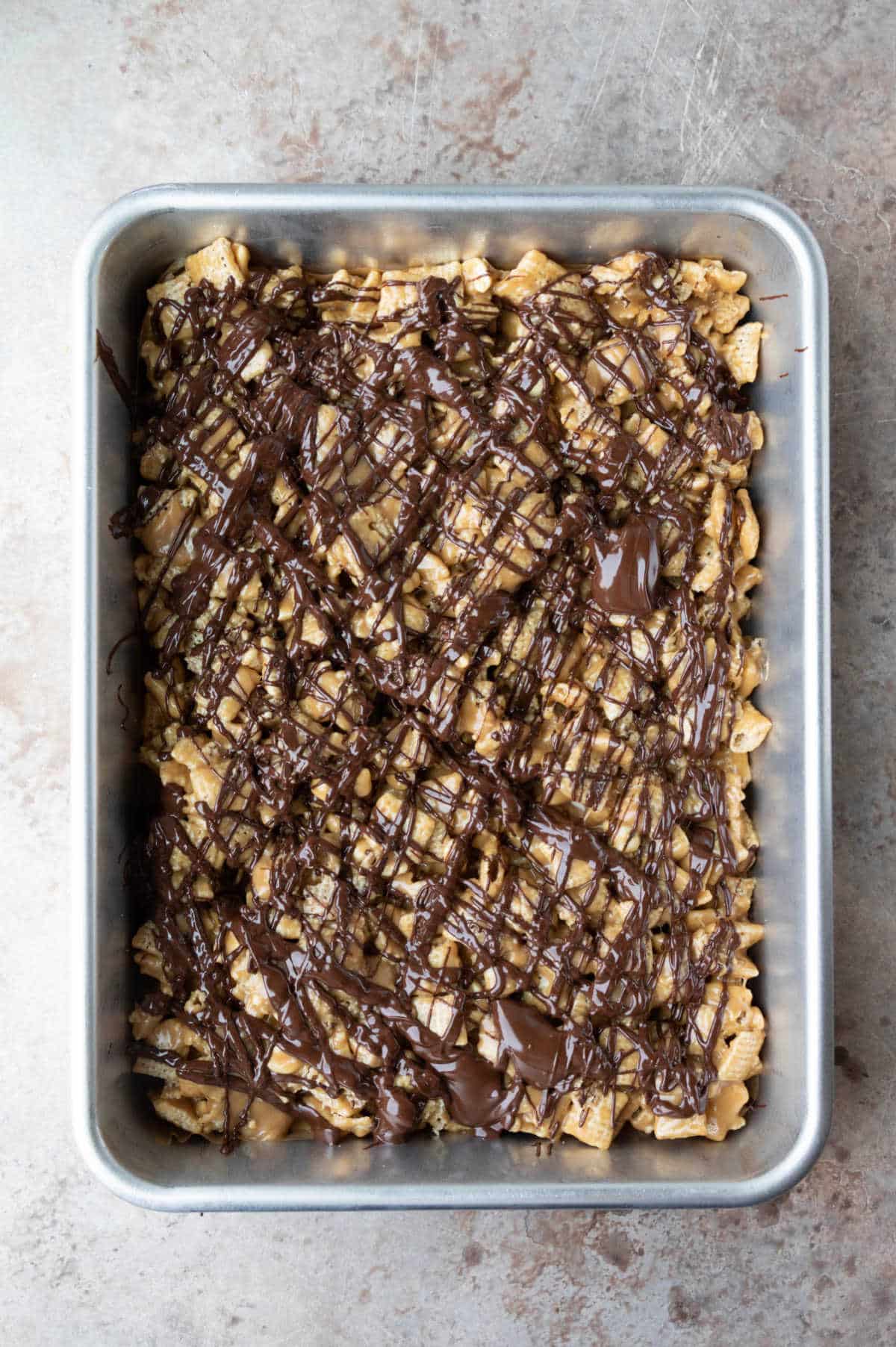 Chocolate drizzled peanut butter Chex cereal treats in a baking pan.