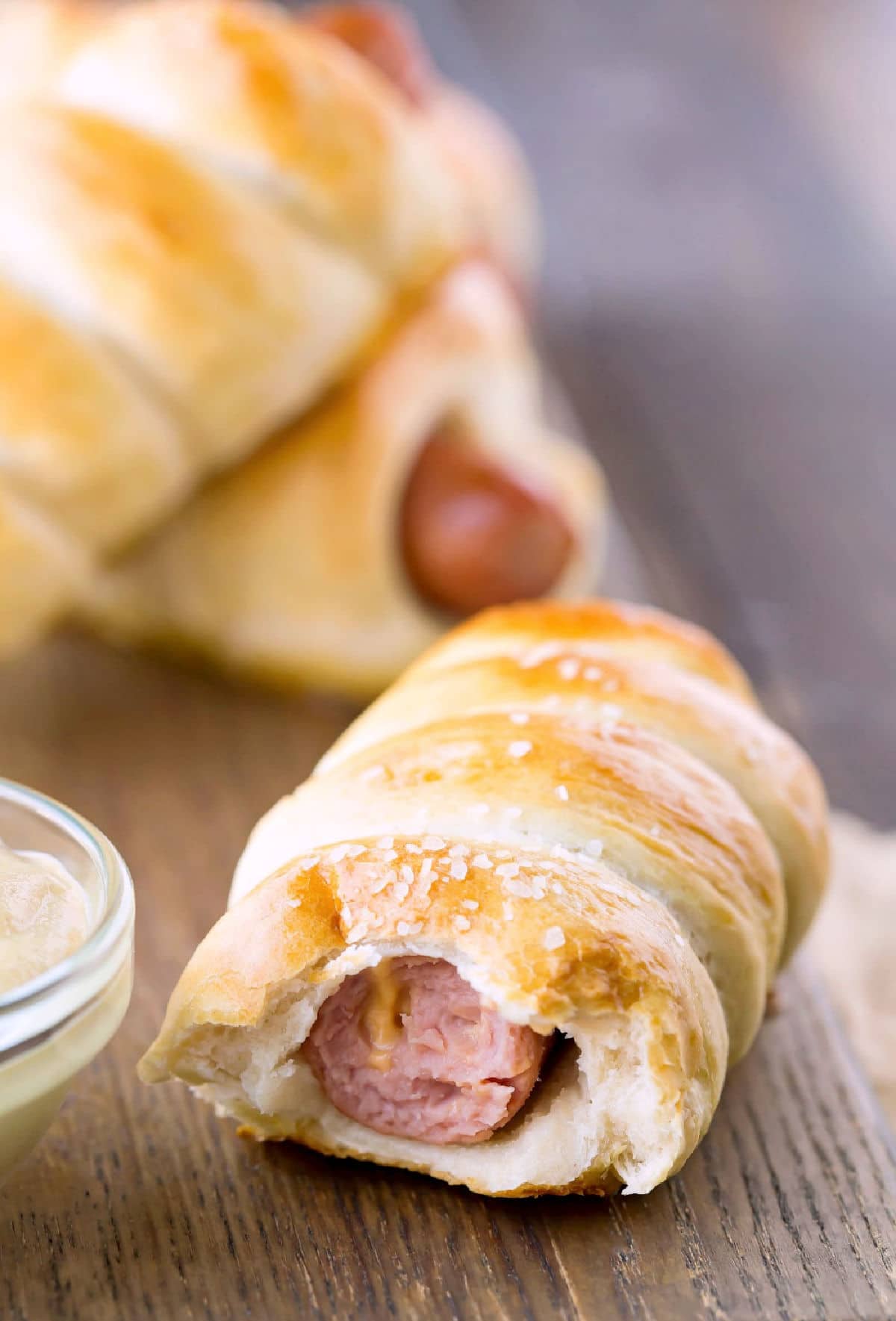 Homemade pretzel dog with a bite missing next to a bowl of mustard. 