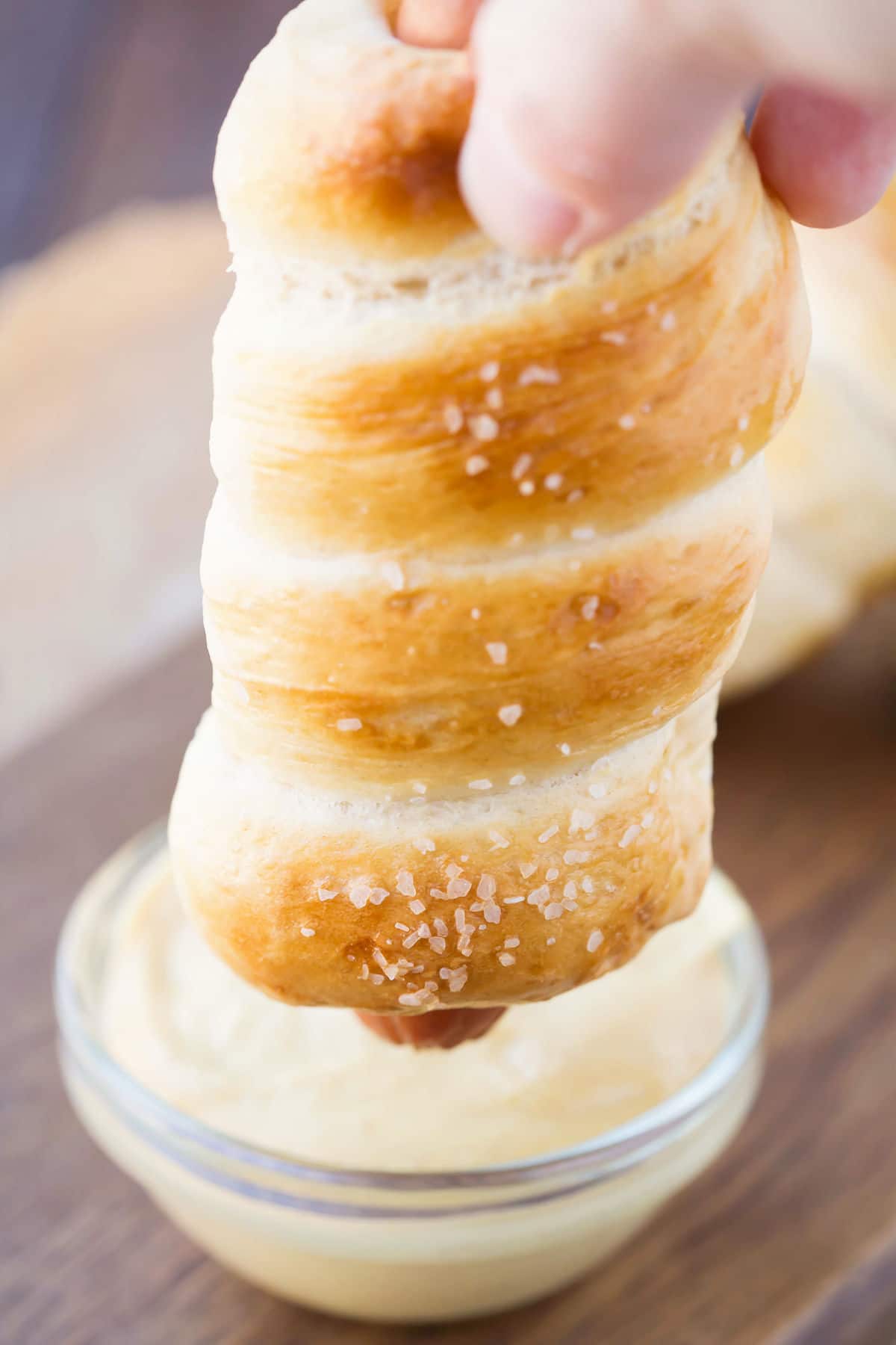 A pretzel dog dipping into cheese sauce. 