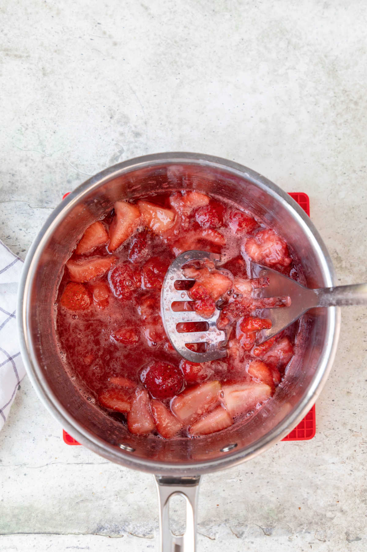 A potato masher mashing strawberries in a saucepan.