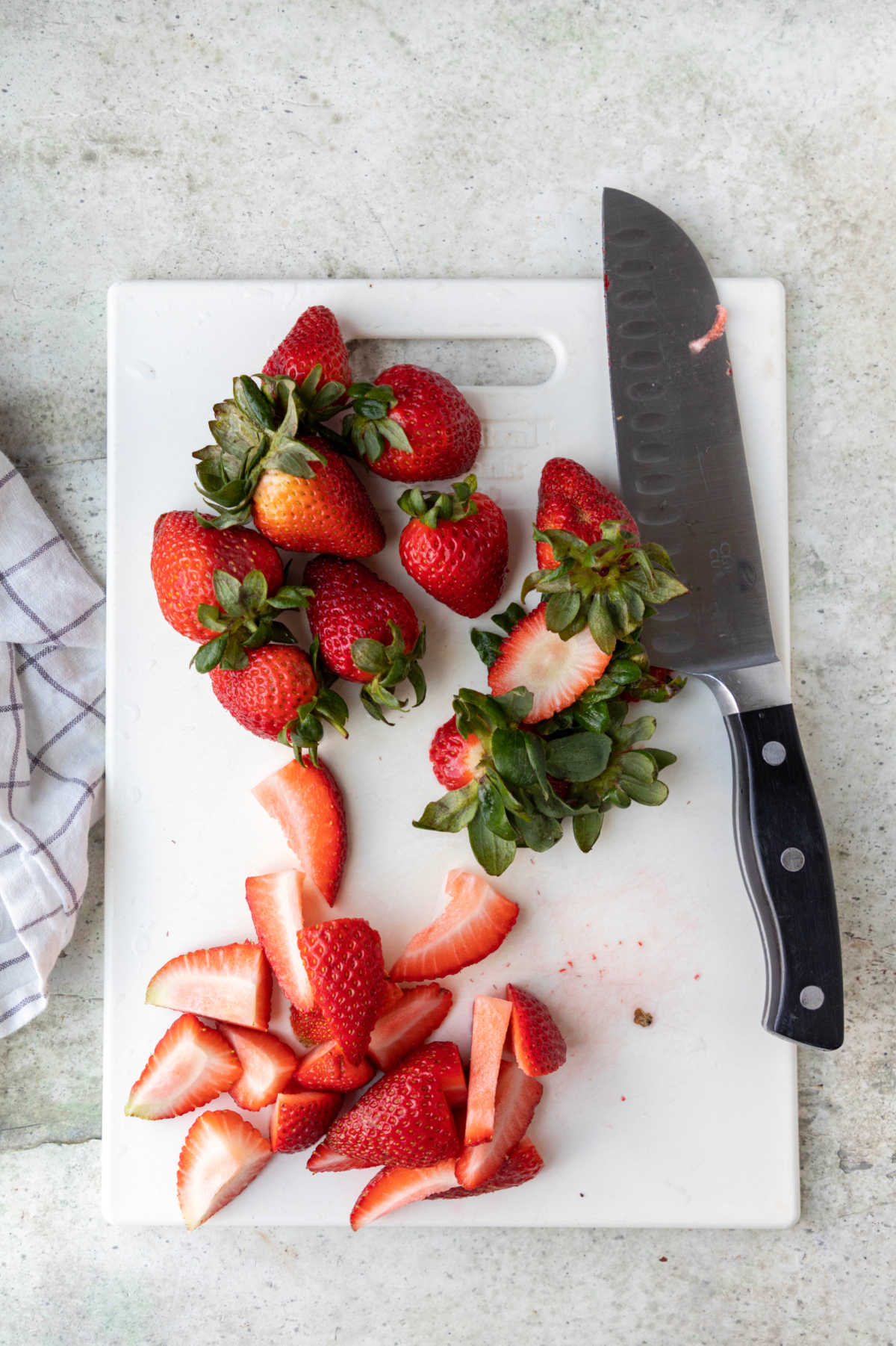 Chopped and whole strawberries on a white cutting board. 