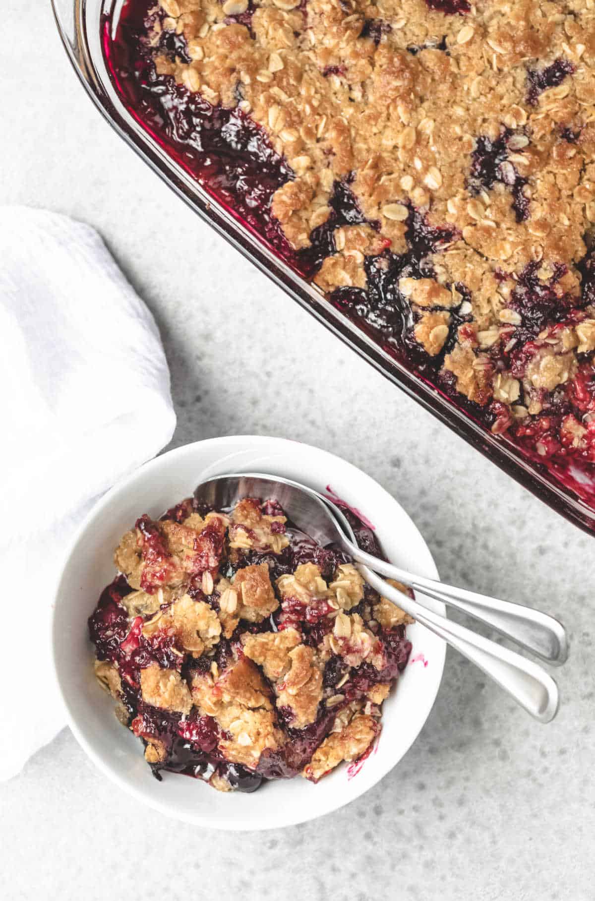 White bowl of triple berry crisp with two spoons in it. 
