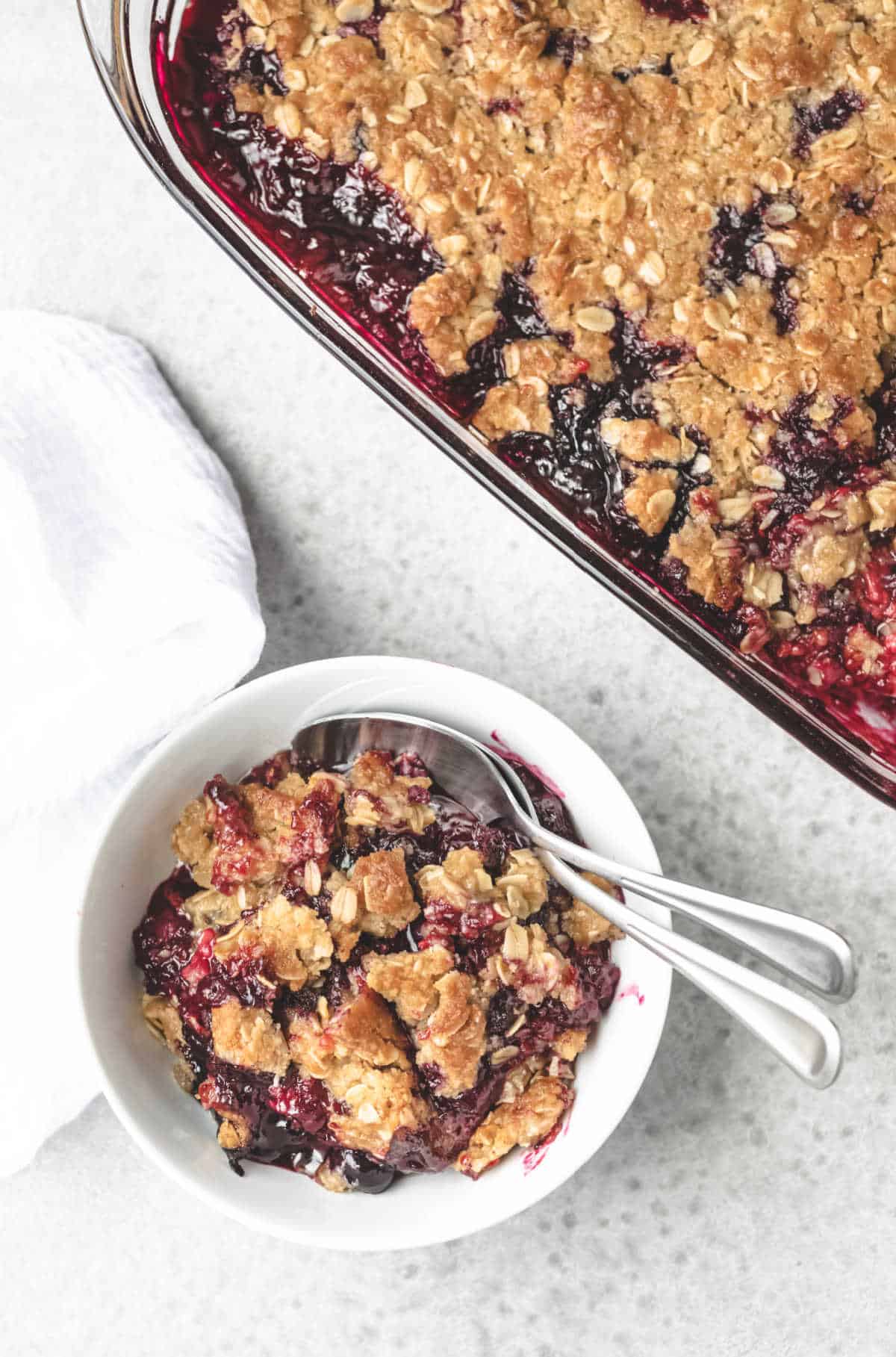 White bowl of triple berry crisp with two spoons in it.