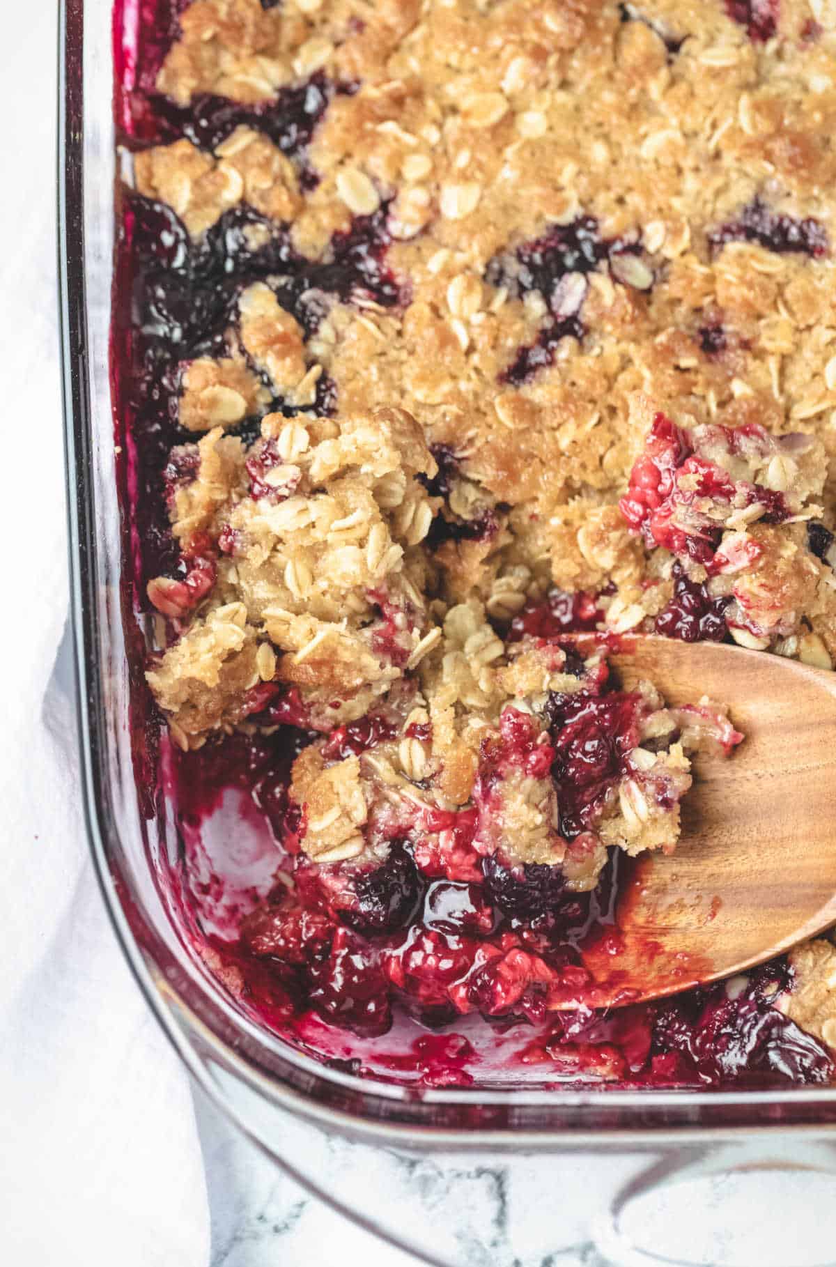 A wooden spoon scooping up triple berry crisp.