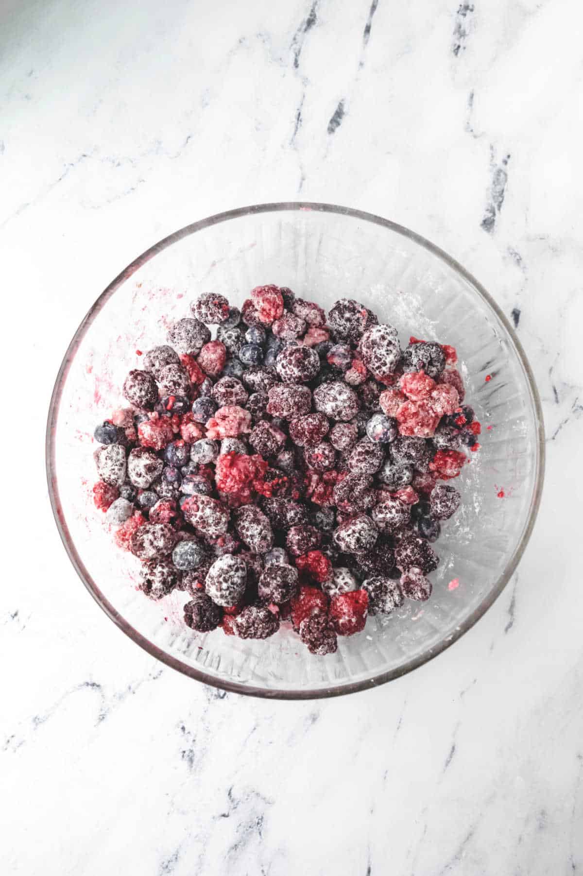 Raspberries blueberries and blackberries in a glass mixing bowl. 