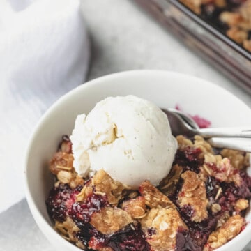 Dish of triple berry crisp topped with a scoop of vanilla ice cream.