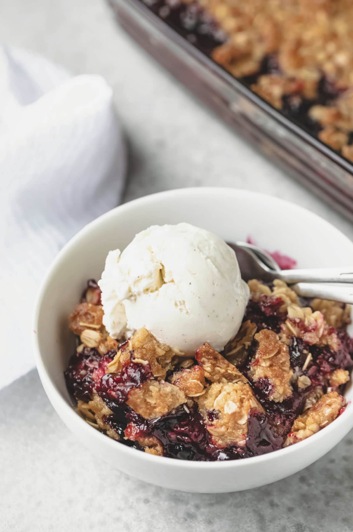 Dish of triple berry crisp topped with a scoop of vanilla ice cream.