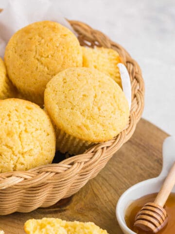 Basket of cornbread muffins next to a dish of honey.