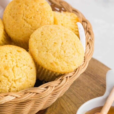 Basket of cornbread muffins next to a dish of honey.