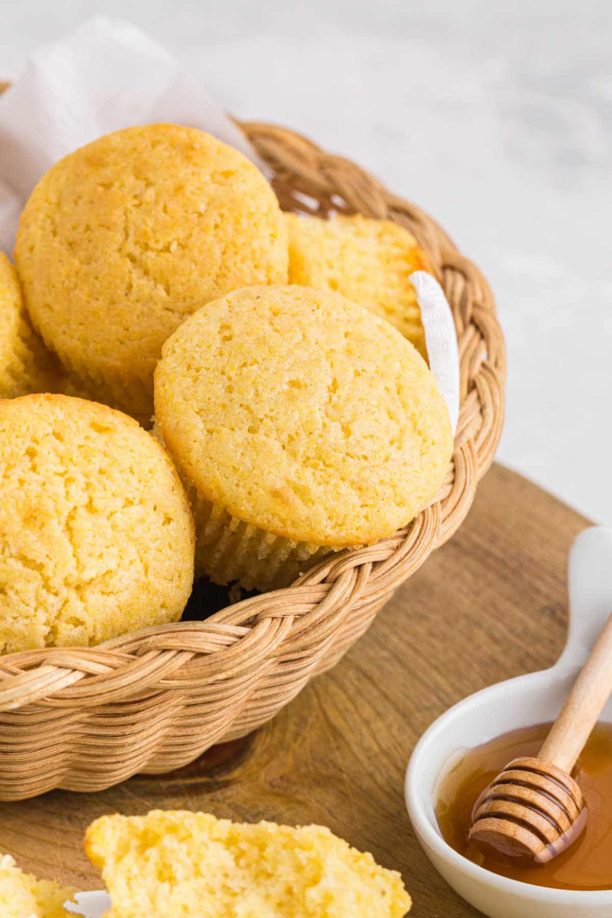 Basket of cornbread muffins next to a dish of honey.